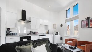A modern kitchen with white cabinets, a black range hood, and a dining area with a table and orange chairs.