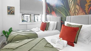 A hotel room with two beds, a large window, a plant, and a colorful wall mural.