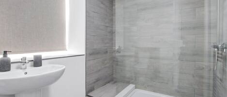 A modern bathroom with a white sink, a glass shower enclosure, and a built-in bathtub.
