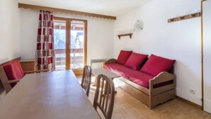 A room with a wooden table, chairs, a red sofa, and a window with curtains.