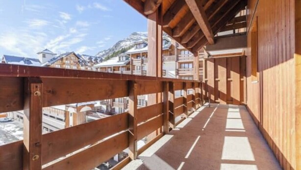 A wooden balcony with a view of snow-covered buildings and mountains.