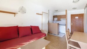 A compact living space with a red sofa, a wooden dining table, and a kitchenette in the background.