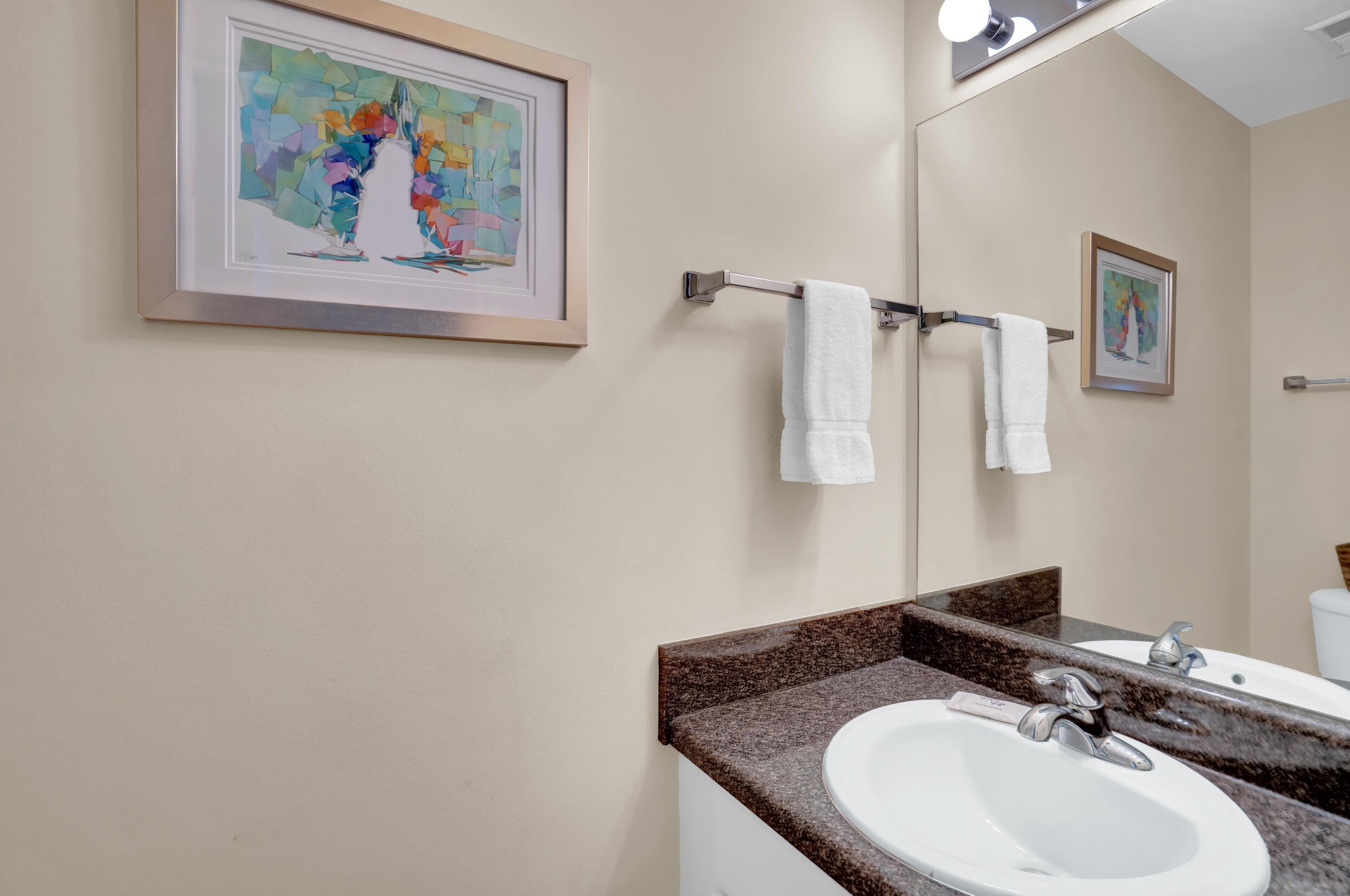 A bathroom with a white sink, a mirror, and two framed artworks on the wall.