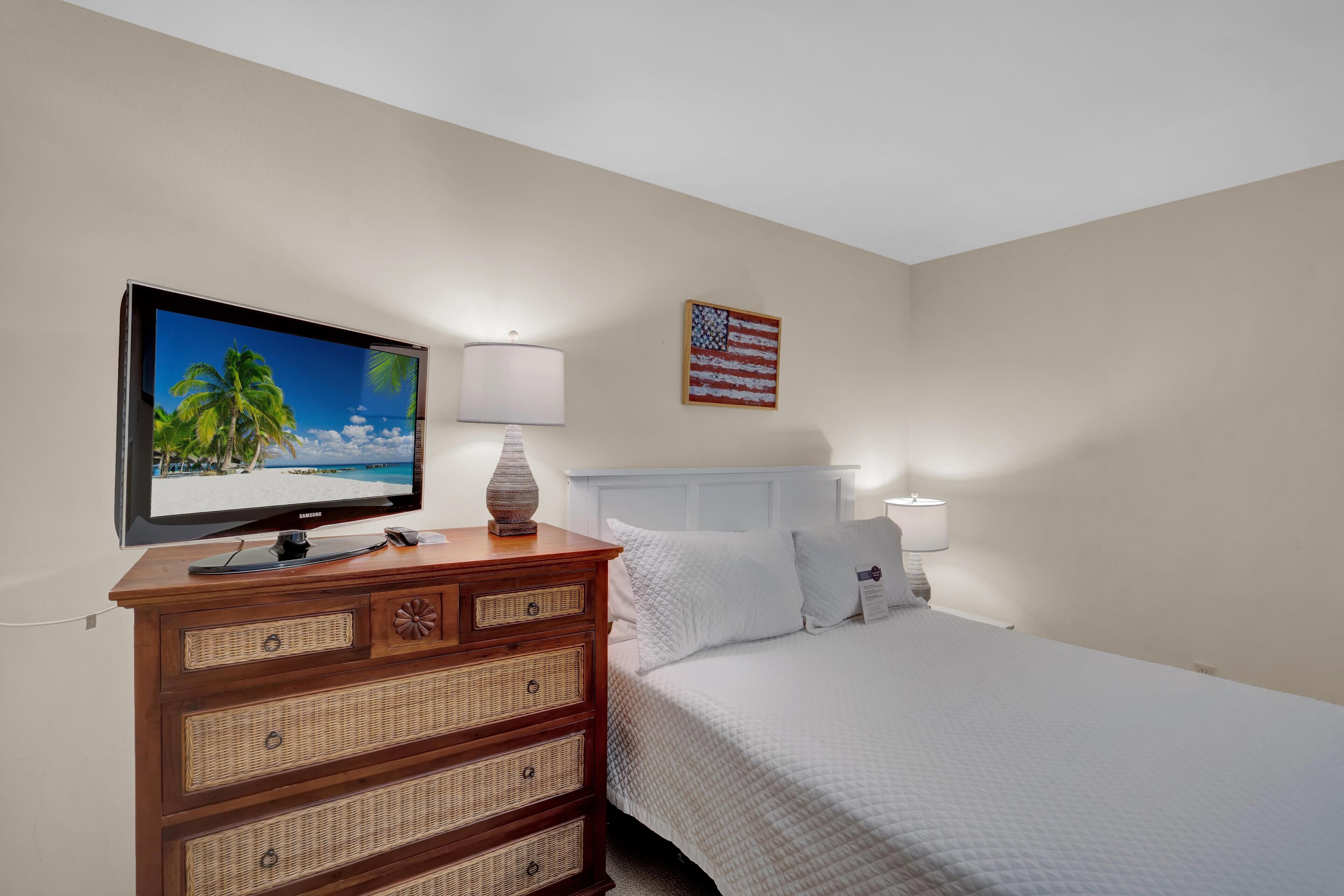 A hotel room with a bed, a television on a wooden dresser, a lamp, and an American flag on the wall.