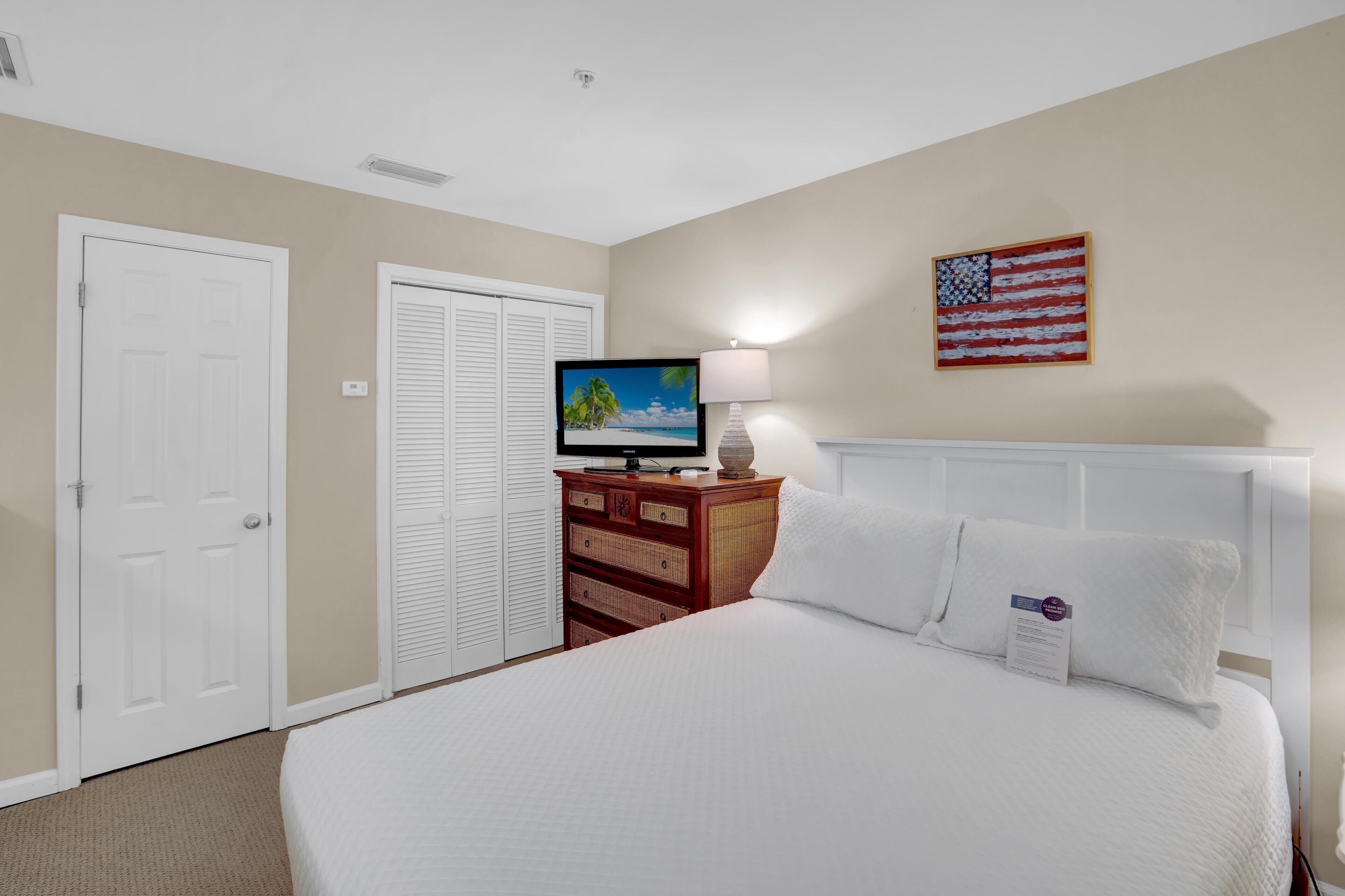 A hotel room with a large bed, a television, a lamp, a dresser, and an American flag on the wall.