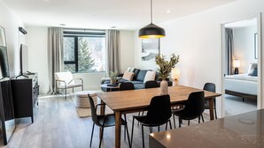 A modern hotel room with a dining area, a sofa set, and a large window with a view of trees. - The Peaks and Birdies (Revelstoke)