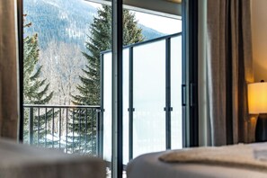 A room with a large window overlooking a forested area and a mountain. - The Peaks and Birdies (Revelstoke)