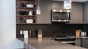 A modern kitchen with a central island, stainless steel appliances, and wooden shelves. - The Peaks and Birdies (Revelstoke)