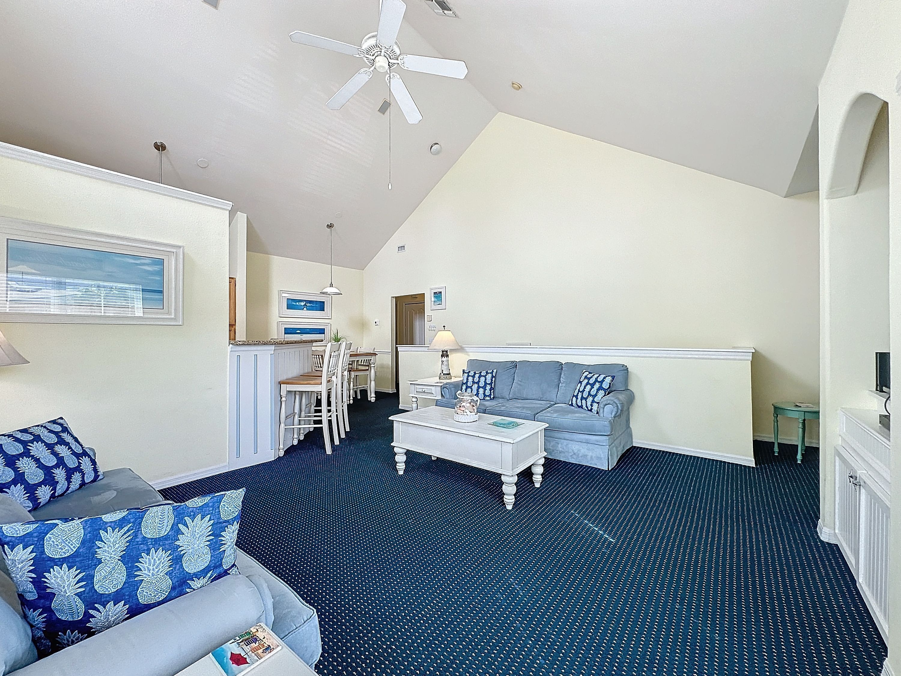 A living room with a blue patterned sofa, a light blue sofa, a coffee table, and a ceiling fan.