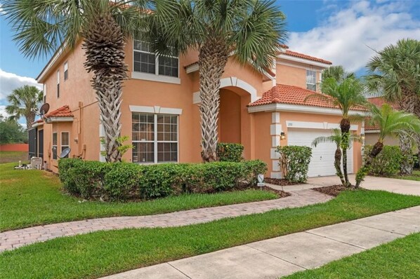 A two-story house with a red-tiled roof, a garage, and a well-maintained lawn with palm trees. - Six Bed Pool Villa in Resort -close to Disney (Davenport)