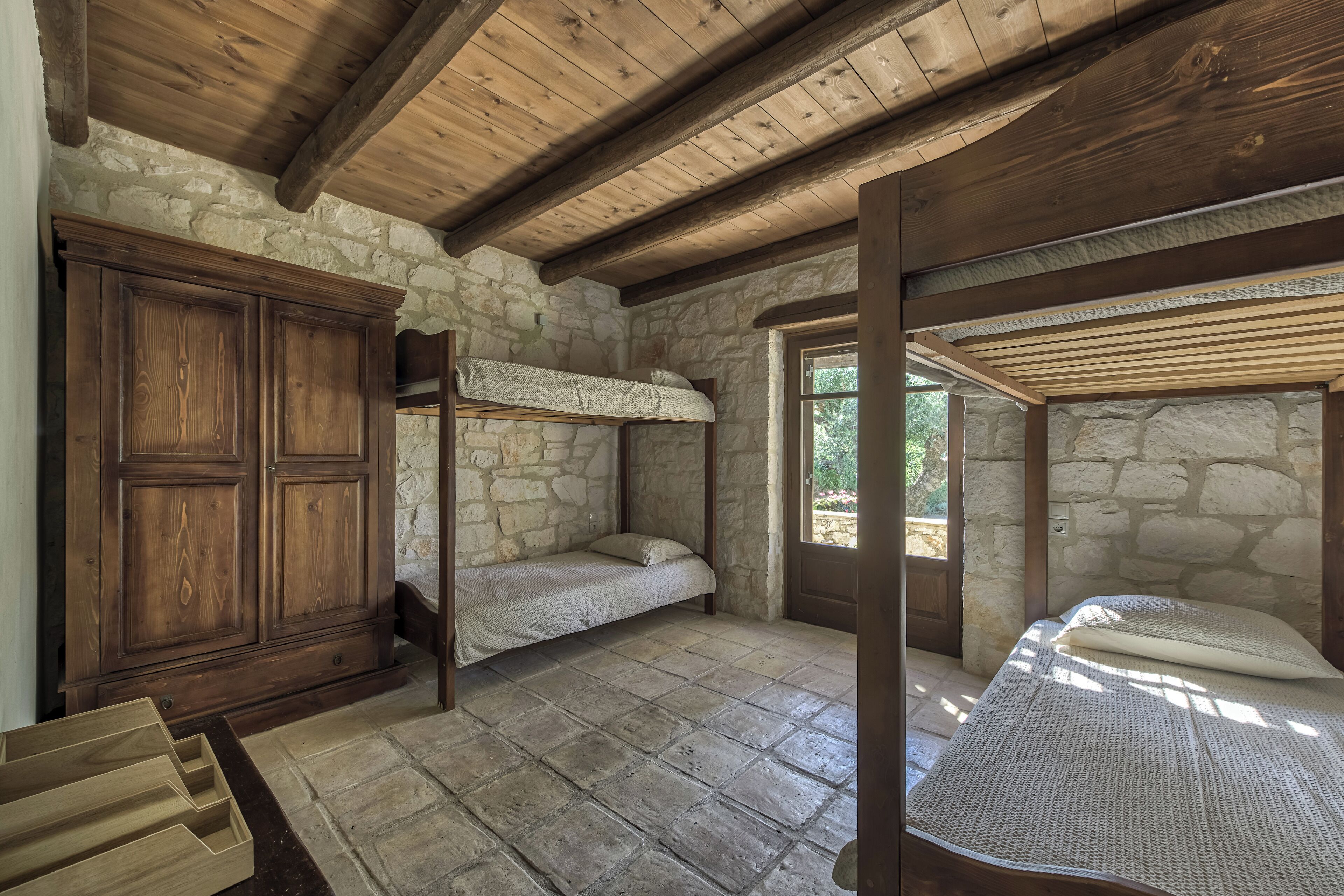 A rustic room with stone walls, wooden ceiling beams, a bunk bed, and a wooden wardrobe.