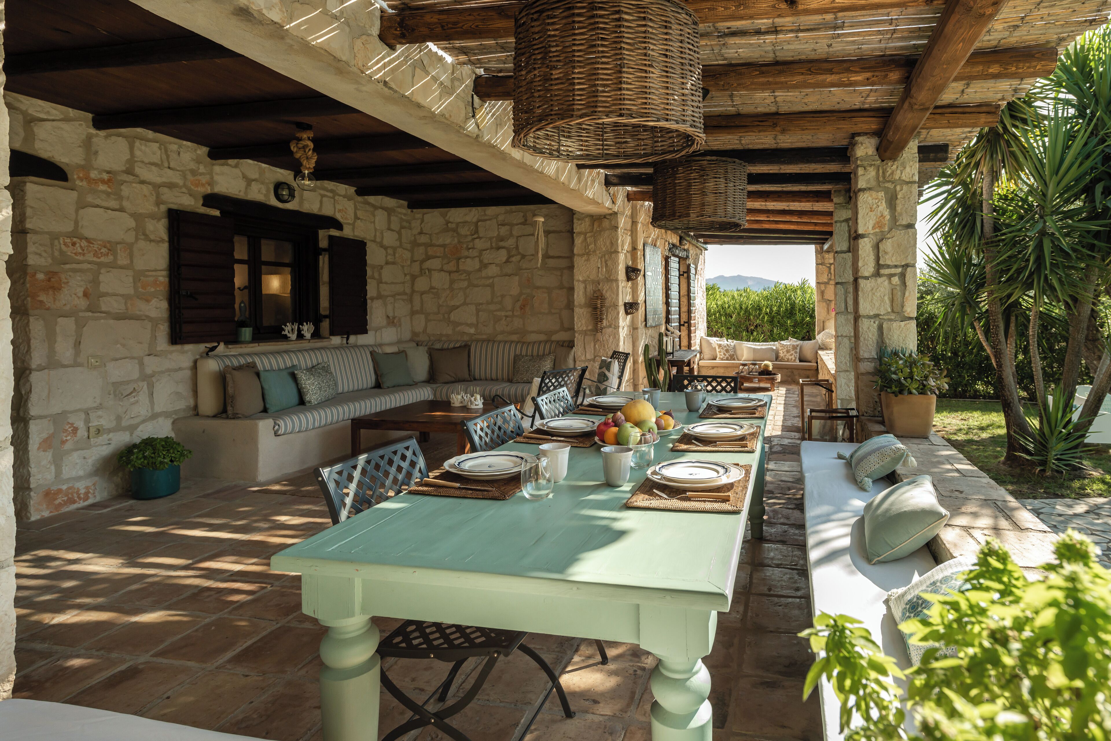 A rustic outdoor dining area with stone walls, wooden beams, and a stone bench.