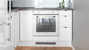 Una cocina moderna con armarios blancos, horno empotrado y piso de madera.