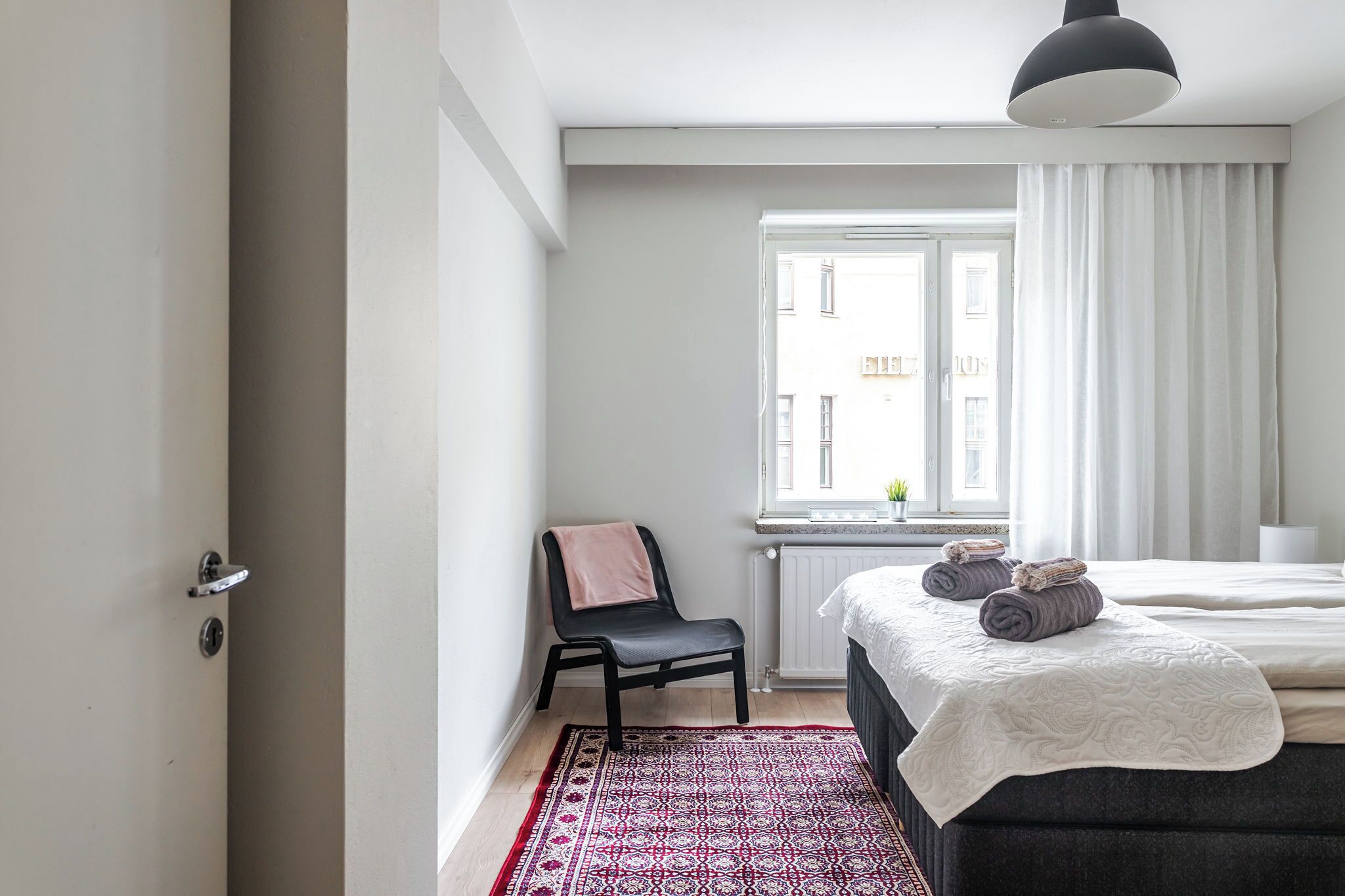 A bedroom with a bed, a chair, a window with curtains, and a radiator.