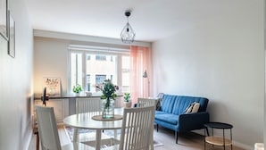 Una sala de estar moderna con un sofá azul, sillas blancas y una mesa de comedor con un florero.