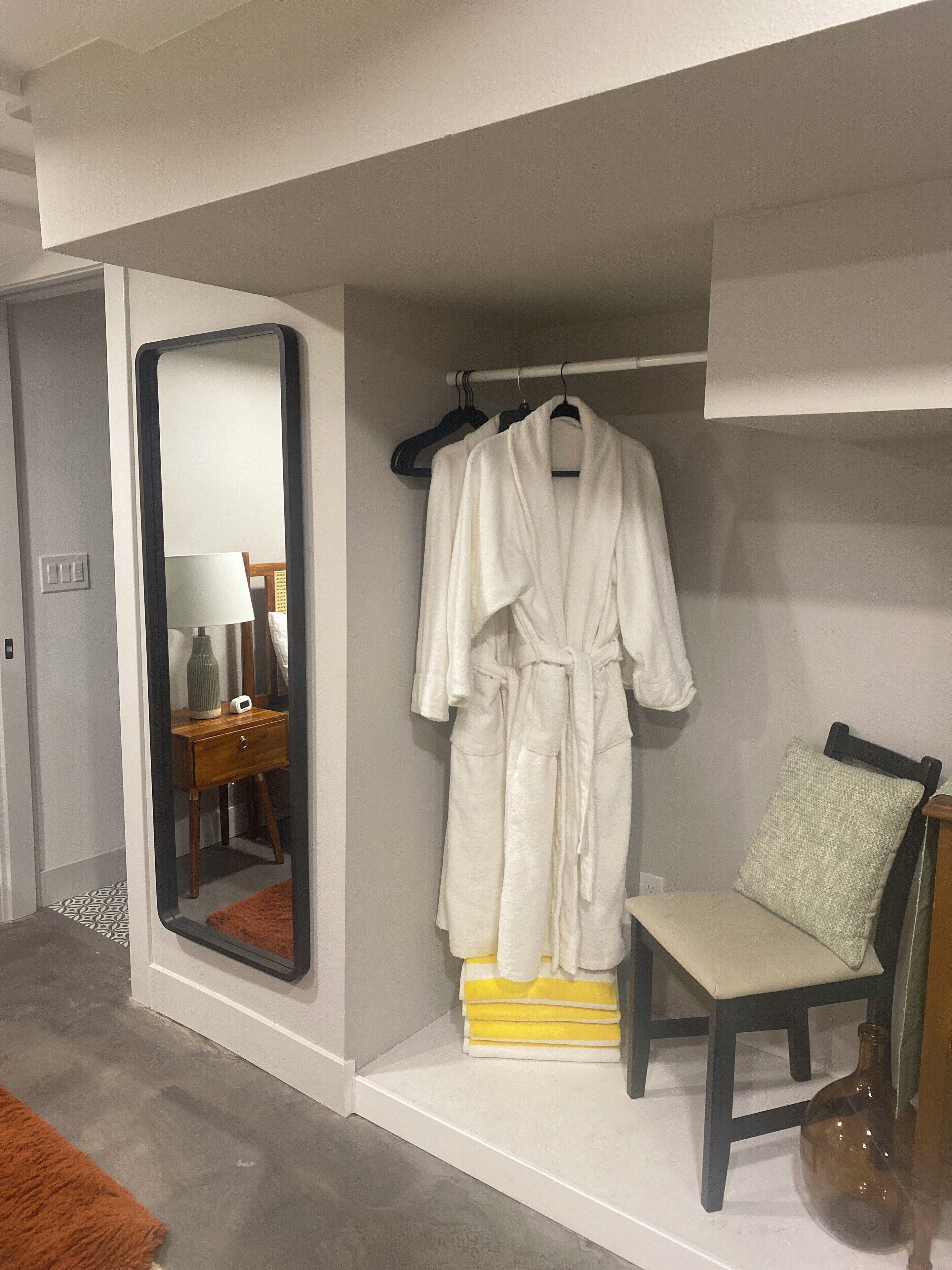 Een badkamer met een spiegel, een badjas, een stoel en een stapel handdoeken.