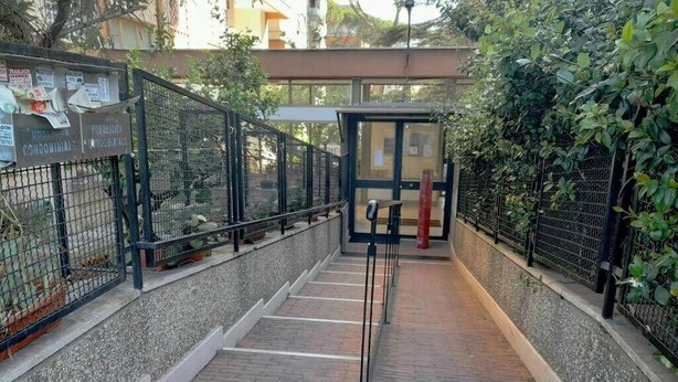 Un pasillo cubierto con barandillas de metal, suelo de ladrillo y una entrada con puerta de vidrio.