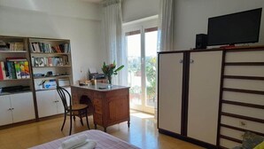 Habitación de hotel con una cama, un escritorio, una estantería, un televisor y vistas al exterior.