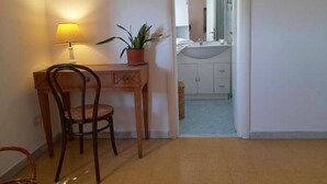 Una habitación con un escritorio de madera, una silla, una planta en maceta y una lámpara.