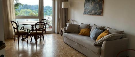 A living room with a sofa, a dining table with chairs, and a painting on the wall.