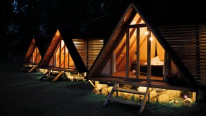 Three wooden triangular cabins with open front doors, each with a bed and a small table. - Hawkay Glamping (Panzaleo)