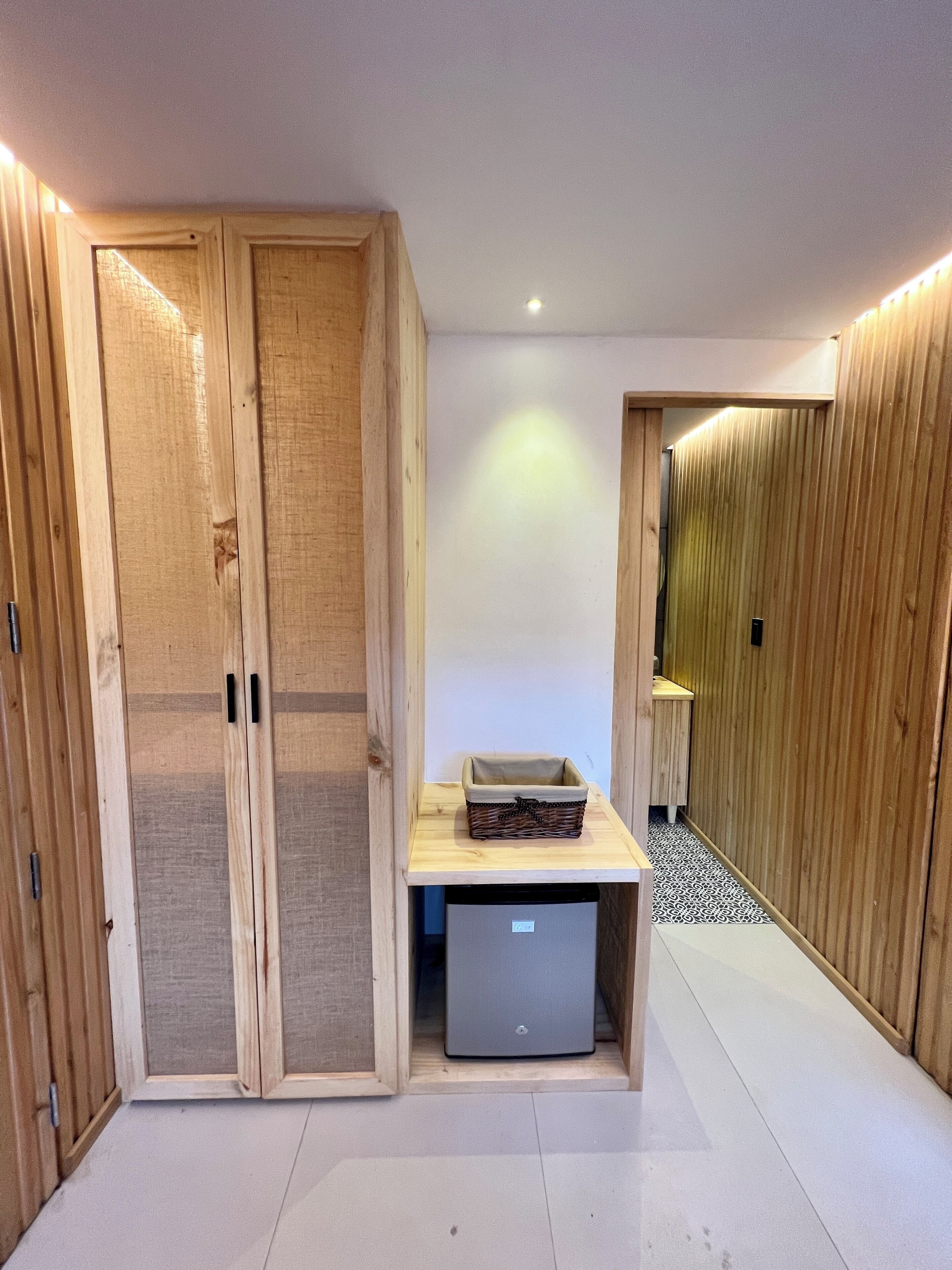Une chambre moderne avec un lambris en bois, une petite table avec un panier et un réfrigérateur compact.