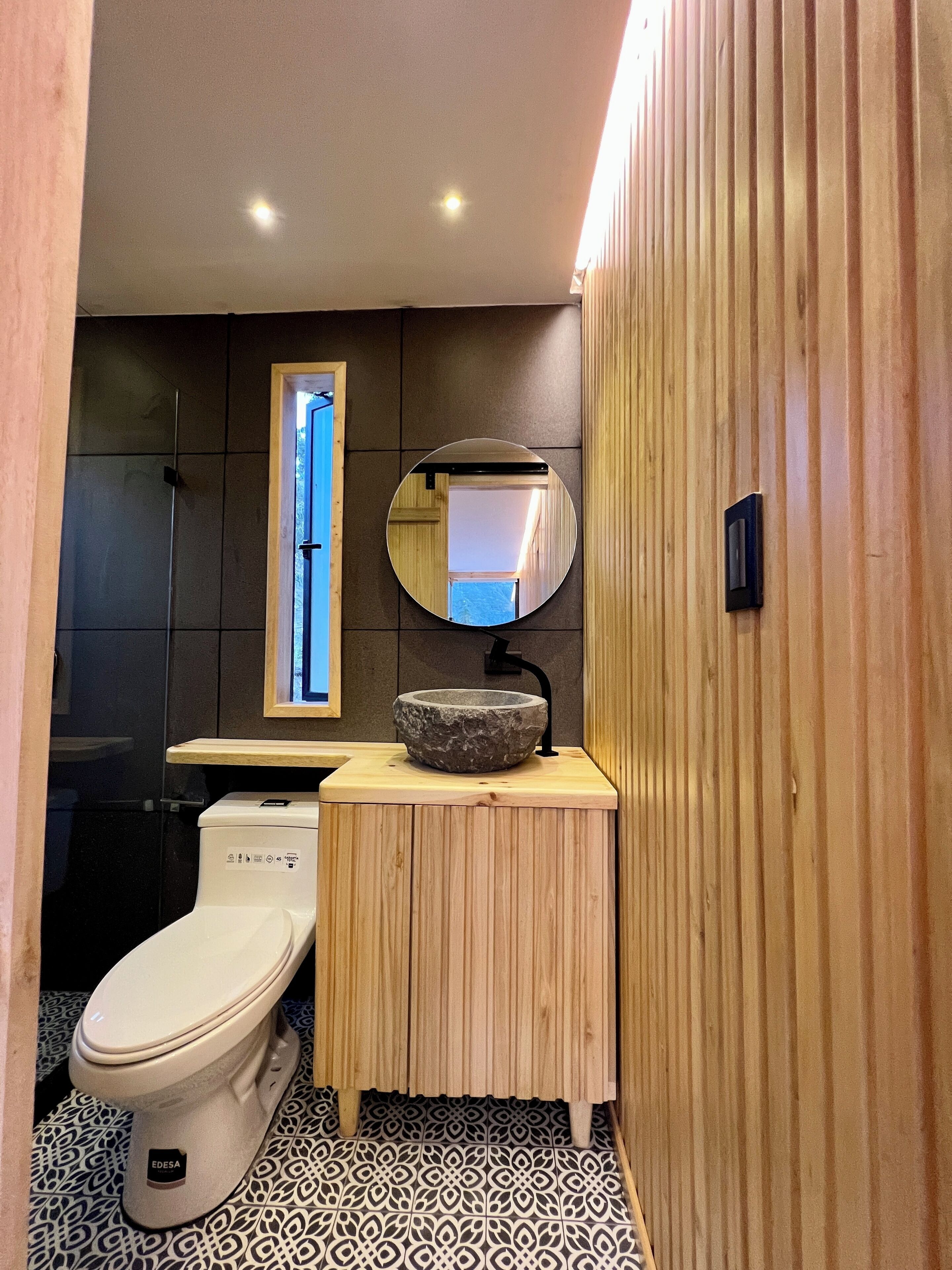 Un baño moderno con un lavabo de piedra, tocador de madera y un inodoro.