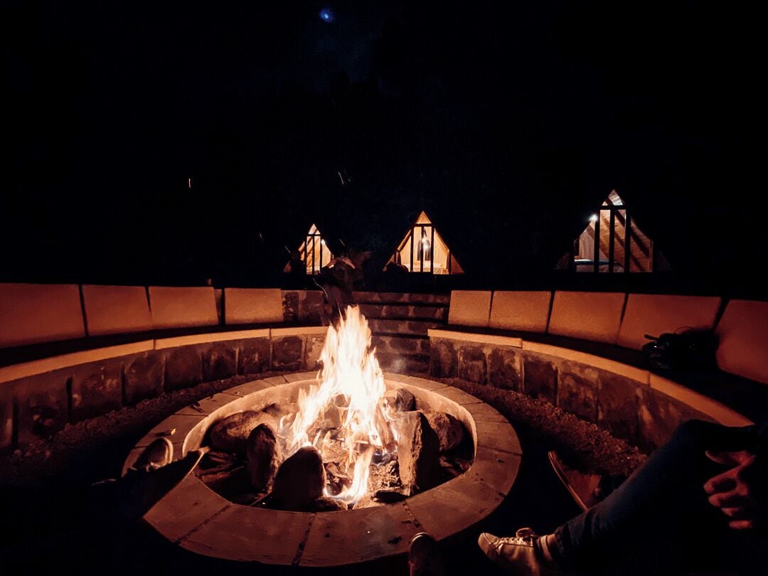 A circular outdoor seating area with a central fire pit, surrounded by stone walls and a low fence.