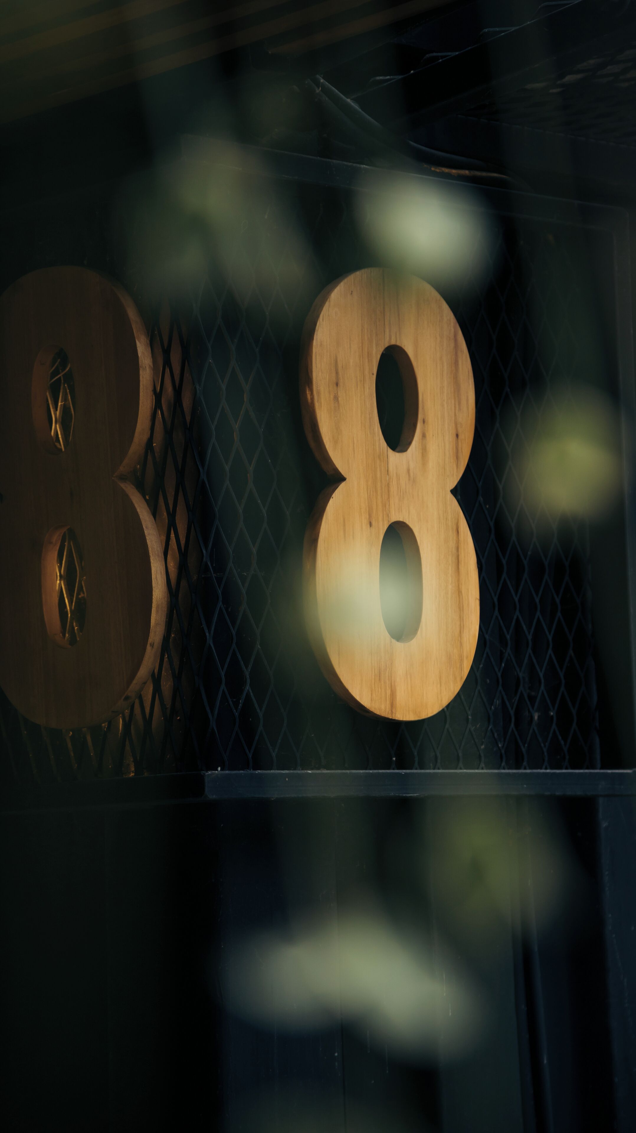 A wooden number '8' sign with a circular cutout, mounted on a metal fence.