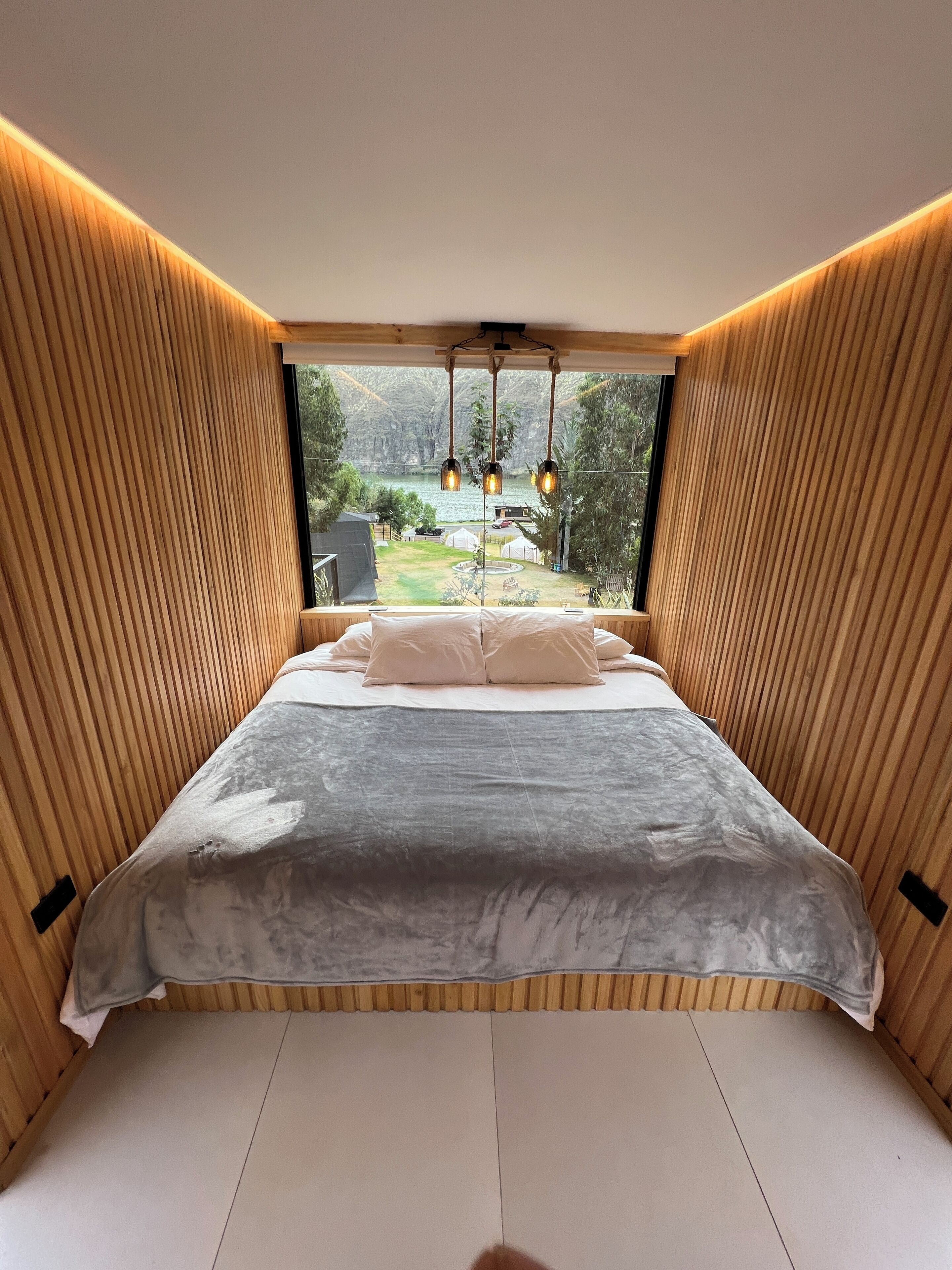 Un dormitorio con una cama grande, paredes de paneles de madera y vistas a un jardín y un lago.