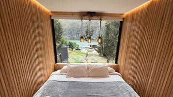 Un dormitorio con una cama grande, paredes de paneles de madera y vistas a un jardín y un lago.