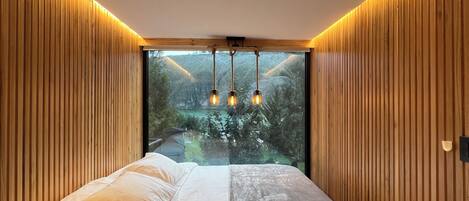 Una camera da letto con un'ampia finestra, pareti in legno a pannelli, un letto con biancheria bianca e una lampada a sospensione.