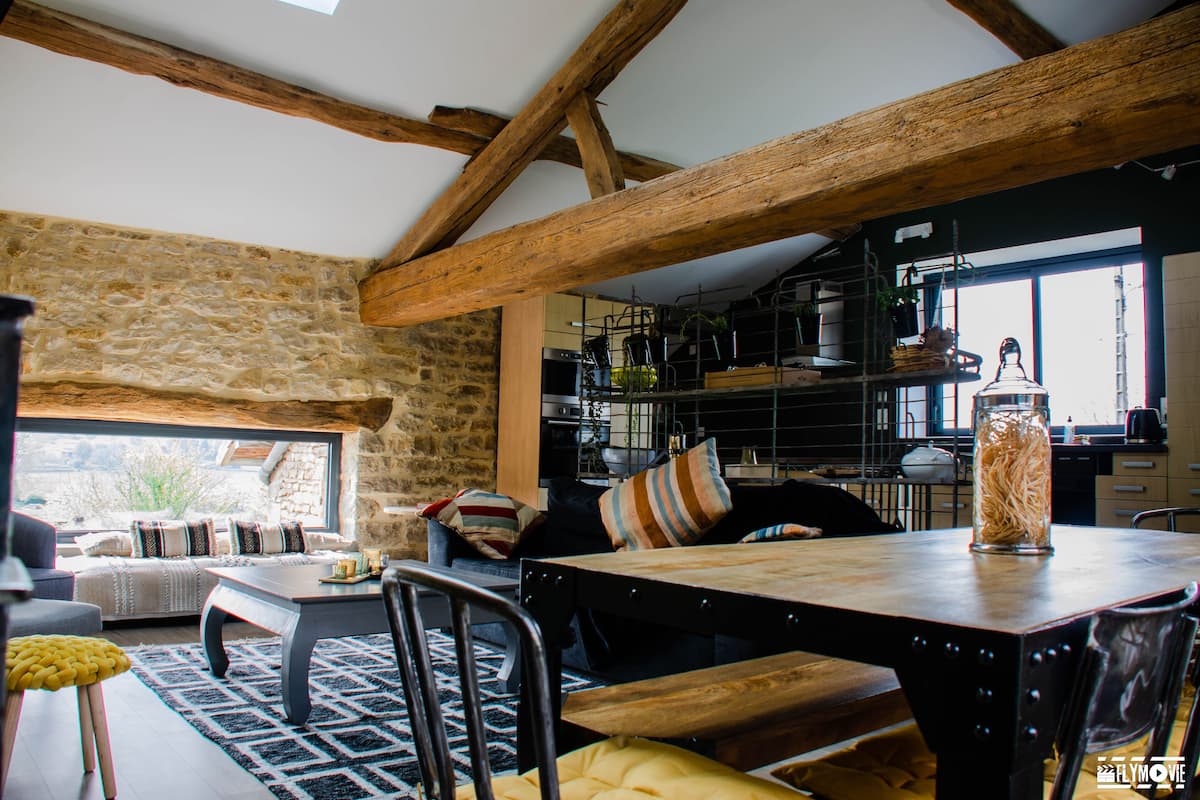 Un interno rustico caratterizzato da travi a vista, un muro in pietra, un'area pranzo con tavolo in legno e una cucina con scaffali ed elettrodomestici.
