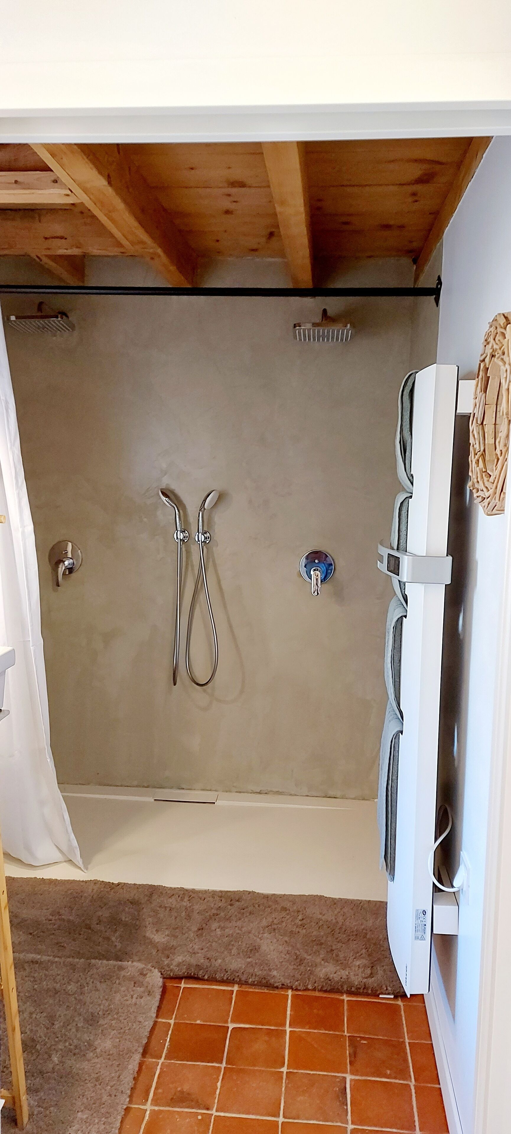 Un petit espace douche fermé, doté d’un plafond en bois, d’un porte-serviettes et d’un mur blanc.