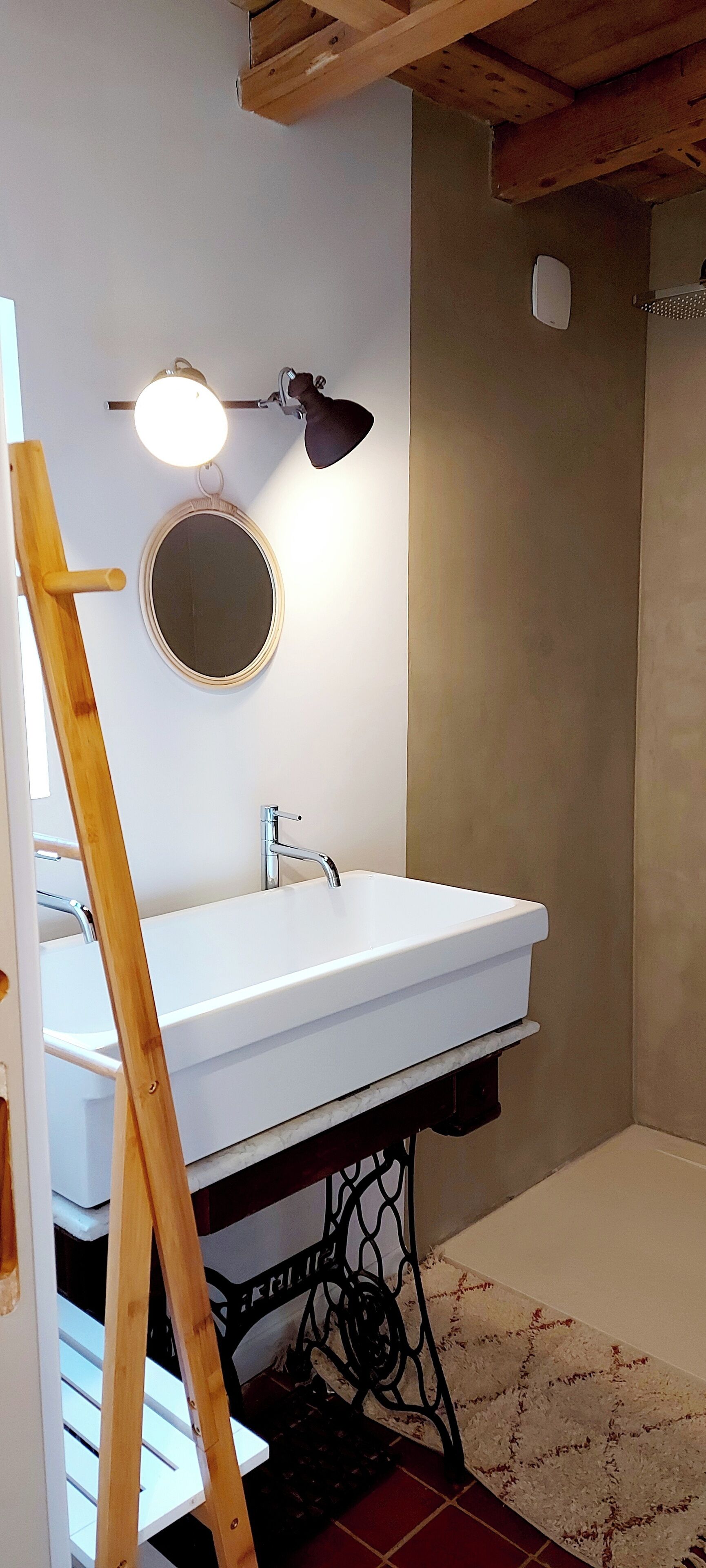 Un baño con un lavabo blanco, un espejo redondo y una escalera de madera.