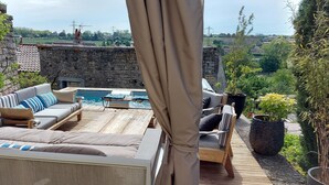 An outdoor seating area with a pool, stone wall, and greenery. - Gîte de La Pyranvôle (Lacrost)