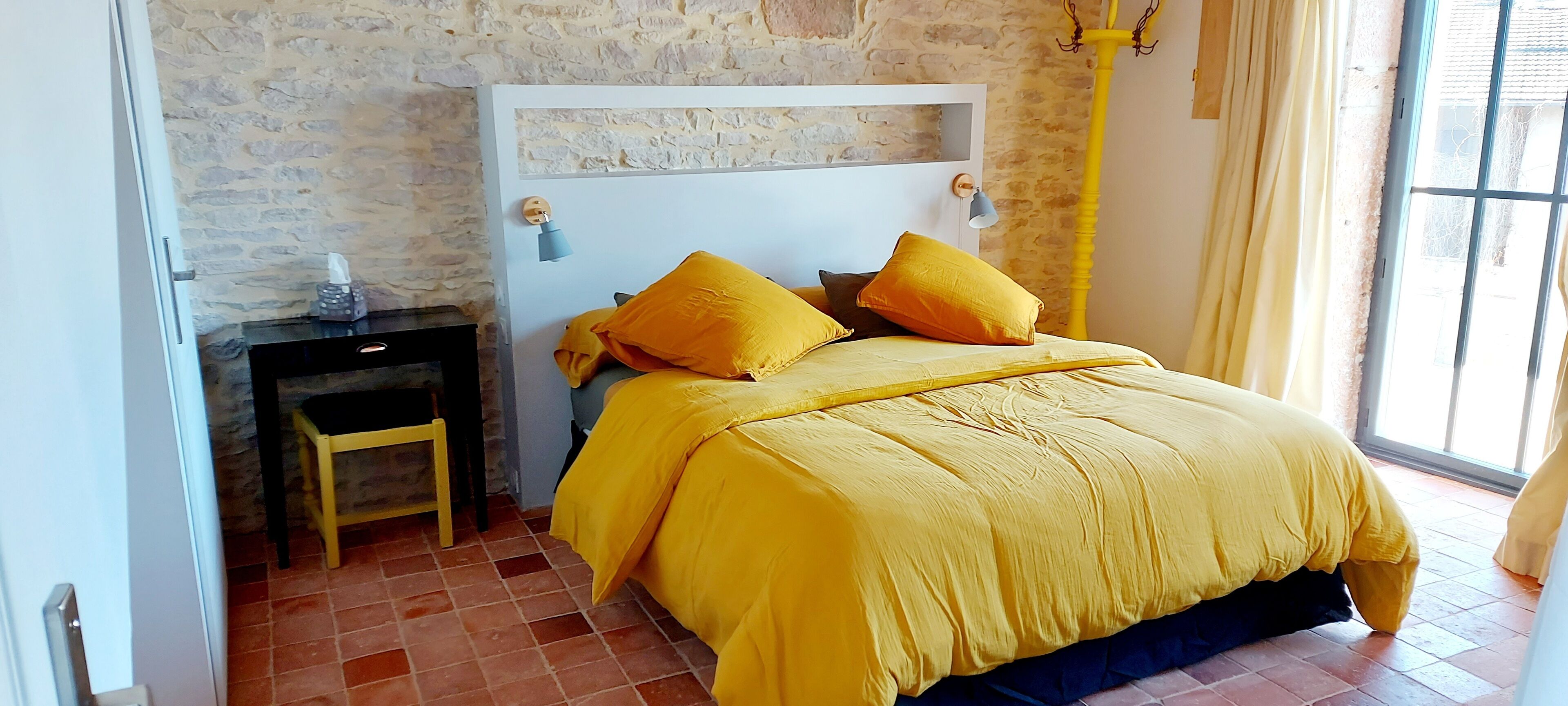 Ein Schlafzimmer mit Steinwand, einem Bett mit gelber Bettwäsche, einem Nachttisch und einem Sessel.
