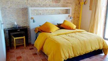 Ein Schlafzimmer mit Steinwand, einem Bett mit gelber Bettwäsche, einem Nachttisch und einem Sessel.