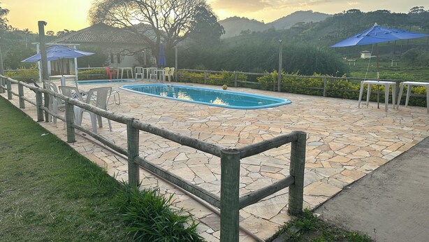 Un espacio al aire libre con pavimento de piedra, una piscina, un cerco de madera y vegetación.