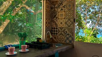 A kitchen with a window overlooking a lush garden, a sink, and a countertop with cups and utensils.