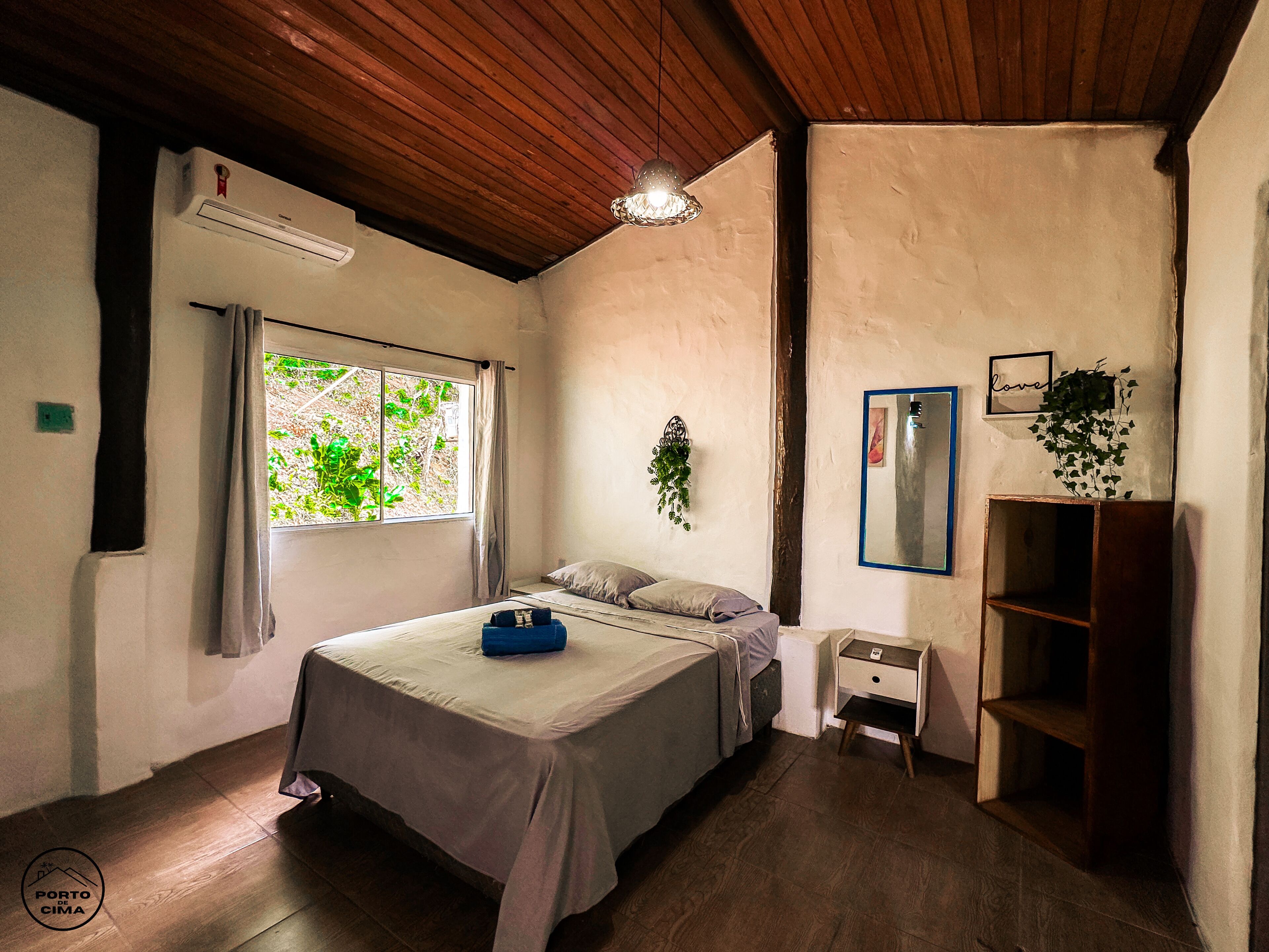 A bedroom with a bed, a nightstand, a shelf, a window, and a ceiling fan.