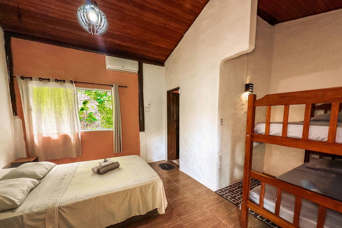 Une chambre à coucher avec un lit, un lit superposé en bois, une fenêtre avec des rideaux et un luminaire au plafond.
