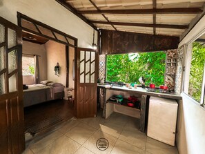 A compact kitchen with a window overlooking greenery, a small dining area, and a sleeping space. - Casas Porto de Cima (Cairu)