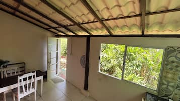 A room with a tiled floor, a dining table with chairs, a window with a view of greenery, and a door leading outside.