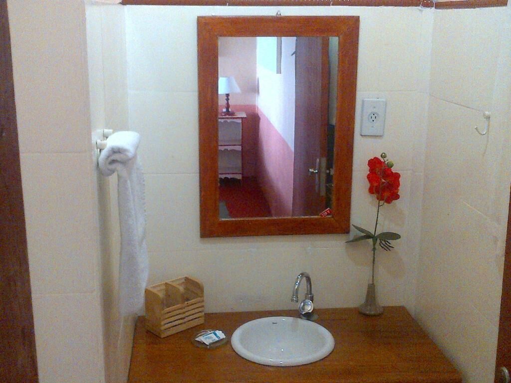Un bagno con un lavandino bianco, un mobile bagno in legno, uno specchio, un portasciugamani e un vaso con un fiore.