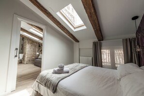 Ein Schlafzimmer mit einer Dachfensterkuppel, einem Bett mit zusammengelegtem Handtuch, einem Heizkörper und Blick auf eine Ziegelwand sowie einen Balkon.