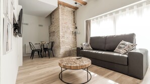 Un salon moderne avec un canapé gris, une table basse ronde en bois et un mur en briques.
