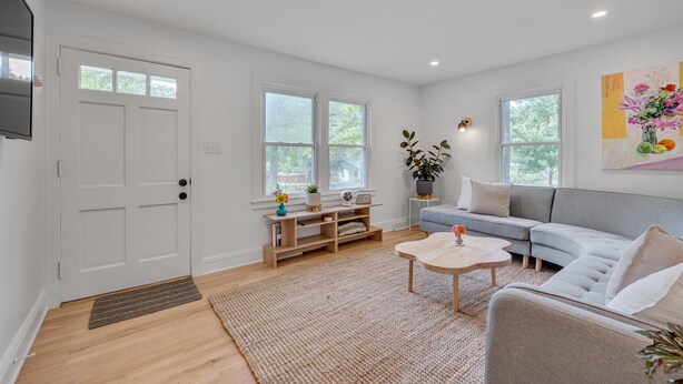 A modern living room with a grey sofa, wooden coffee table, and a TV mounted on the wall.