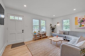 Ein modernes Wohnzimmer mit grauem Sofa, Couchtisch aus Holz und einem an der Wand montierten Fernseher.