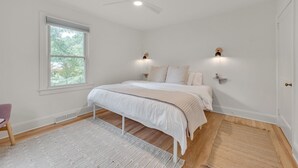 A bedroom with a bed, a ceiling fan, a window, and a nightstand with a lamp.
